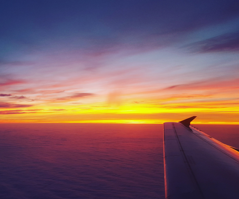 An airplane wing above clouds beneath a vivid sunset sky.