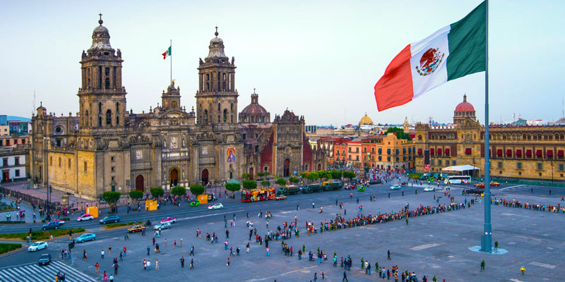 A cathedral, a large Mexican flag and pedestrians in a historic Mexico City square.