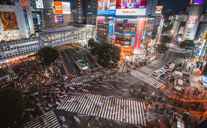 Crowds crossing a brightly lit Tokyo intersection beneath illuminated billboards.